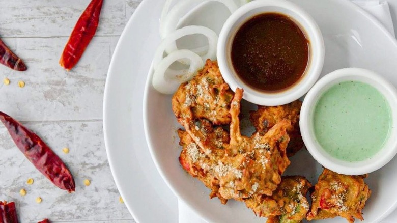 Crispy pakodas with dipping sauces on a white plate on a table decorated with peppers