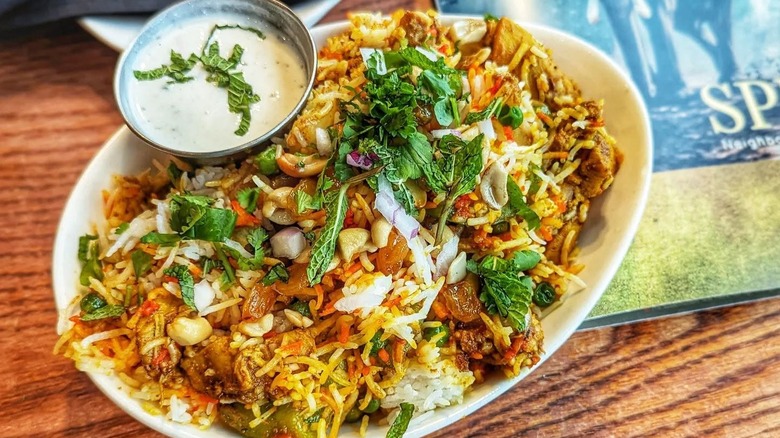 Biryani on a white plate garnished with fresh mint with a side of cucumber raita from Spice Room