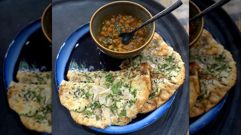 A chickpea curry in a bowl with a black spoon and naan bread for dipping at Masala Kitchen