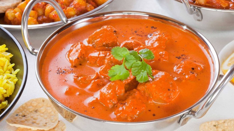 A buttery Indian curry in a metal serving bowl garnished with cilantro