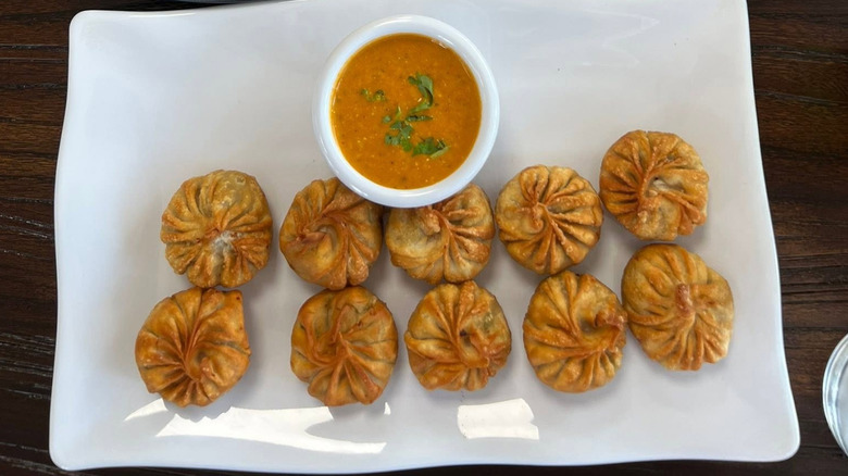 A white plate full of momos and a dipping sauce