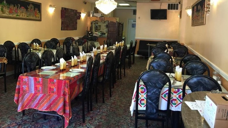 The hole-in-the-wall interior of Jewel of India restaurant with several tables lined with colorful tablecloths and black chairs