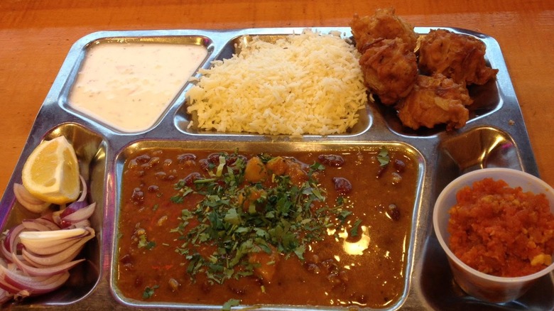 Thali with rice, a bean, curry, red onion, lemon, and pakoras