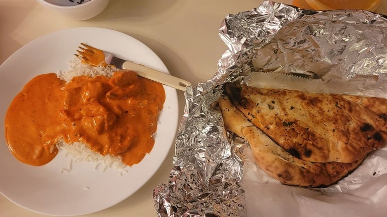 Curry and rice on a white plate and naan on aluminum foil