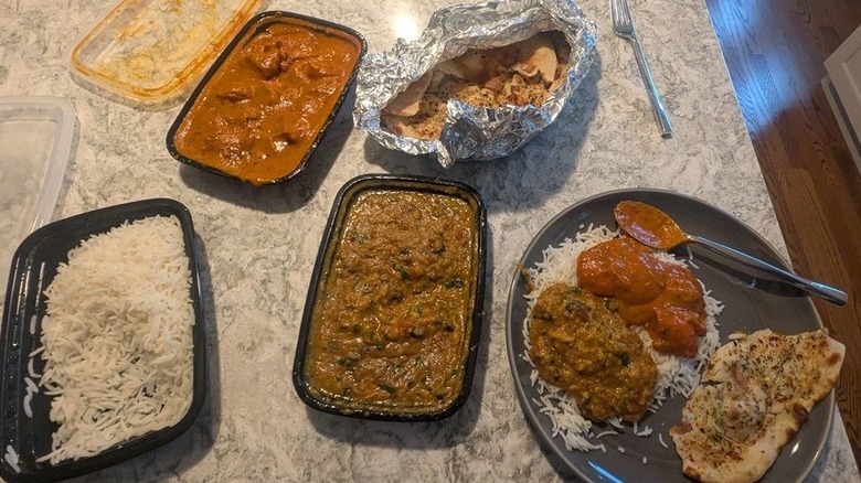 A spread of curries, rice, and naan in to-go containers and dished out on a black plate from Trexler Indian Curries