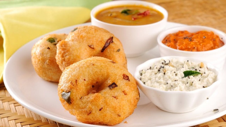Savory Medu Vada, fried lentil donuts, with dipping sauces and curry from Chennai Express on a white plate