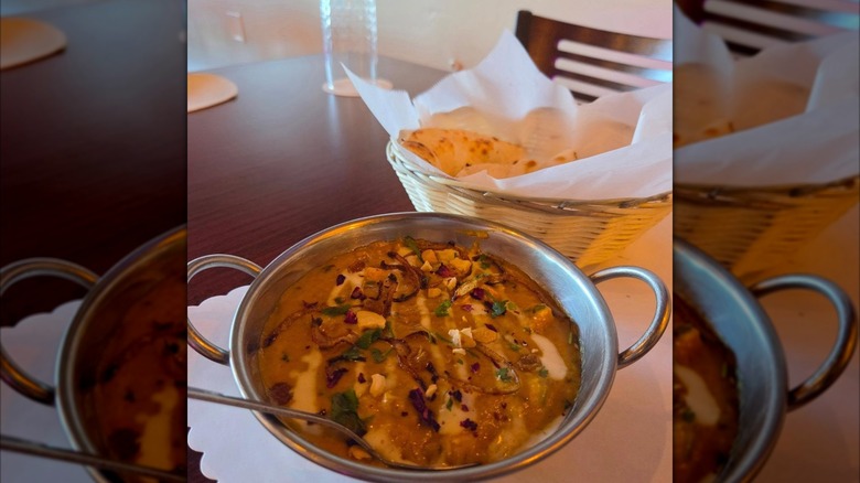 An Indian curry in a metal serving bowl with naan on the side from Slc Dhaba