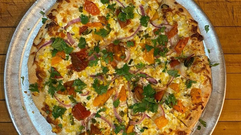 Whole pizza with vegetables, pepperoni, and fresh herbs from baked