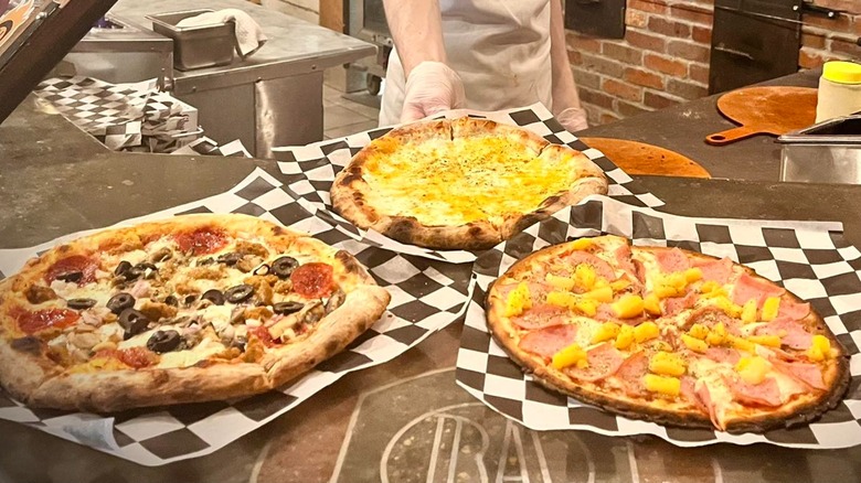 Three different pizzas displayed on the counter at Back Alley Pizza
