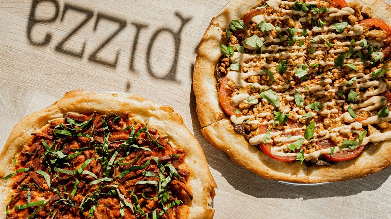 Two whole pizzas with fresh greens and tomato and sauces from Secret Pizza Society