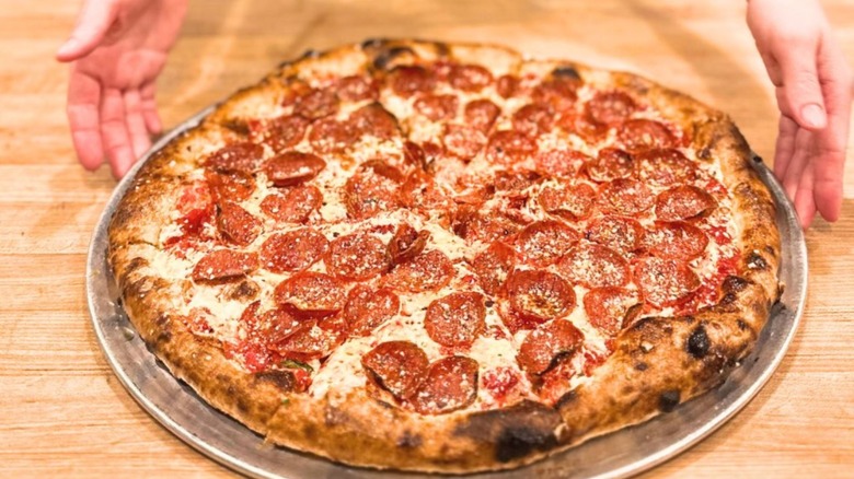 A woman´s hands setting out a whole pepperoni pizza on sourdough crust from Smith and Lentz