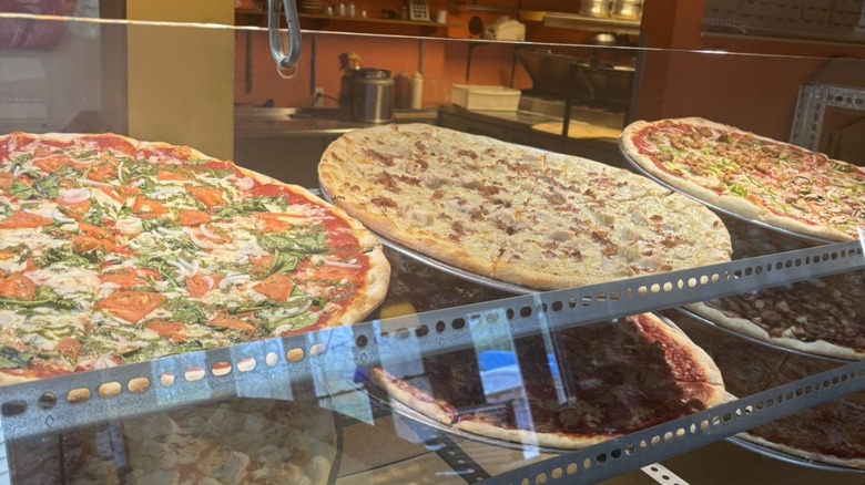Various whole pizzas on display on a rack behind a glass window at iPie Pizzeria