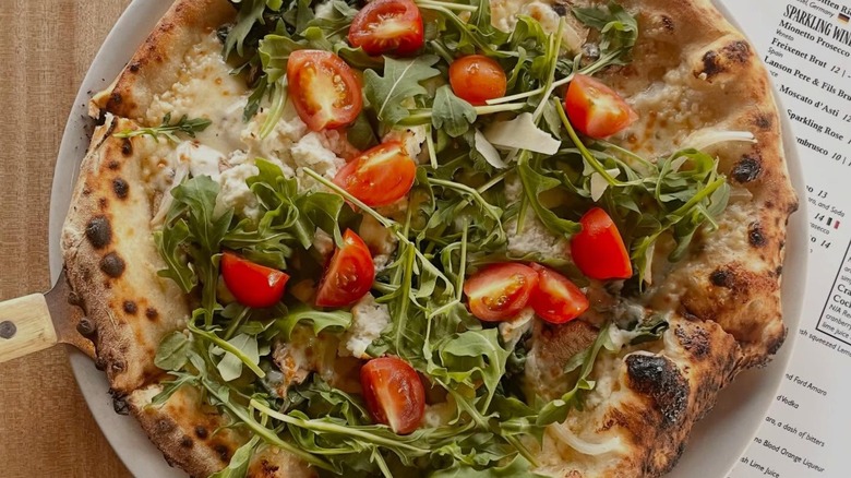 Whole wood-fired pizza with fresh tomato wedges, greens, and cheese from Santino's Little Italy 