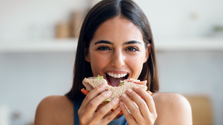 a woman smiling and tasting a sandwich