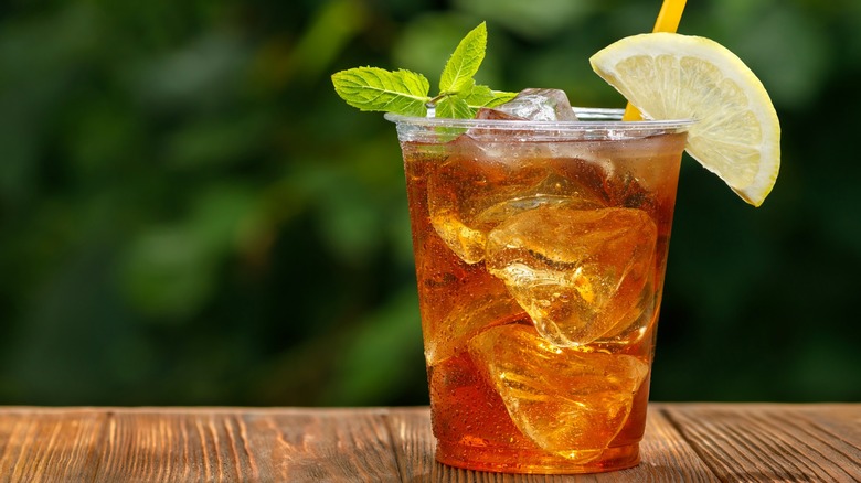 Plastic cup with iced tea, lemon slice, and mint sprig on wooden table