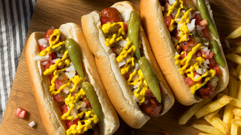 three Chicago-style hot dogs on a board with fries