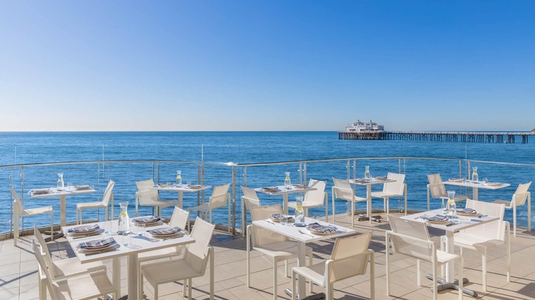 White tables and chairs on an outdoor patio overlooking the ocean with a jetty in the distance