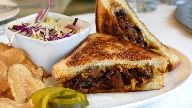 A beef brisket sandwich with a tub of coleslaw, chips, and pickles