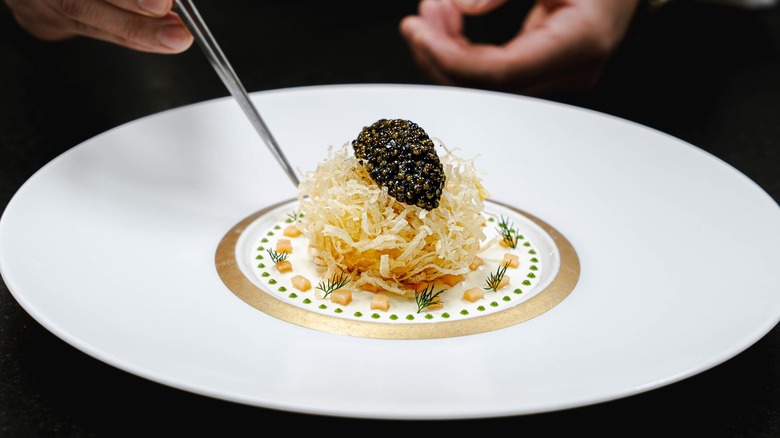 A chef with tweezers adds the finishing touches to a plate of food