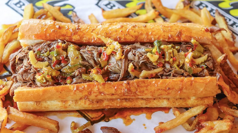 A Italian beef sandwich sits surrounded by fries on signature Al's sandwich wrapping paper.