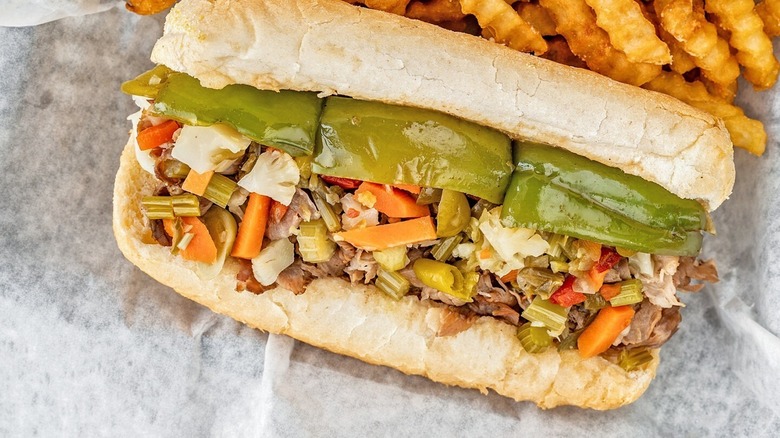 An Italian beef sandwich sitting on a wrapper, crinkle fries to the right of it.