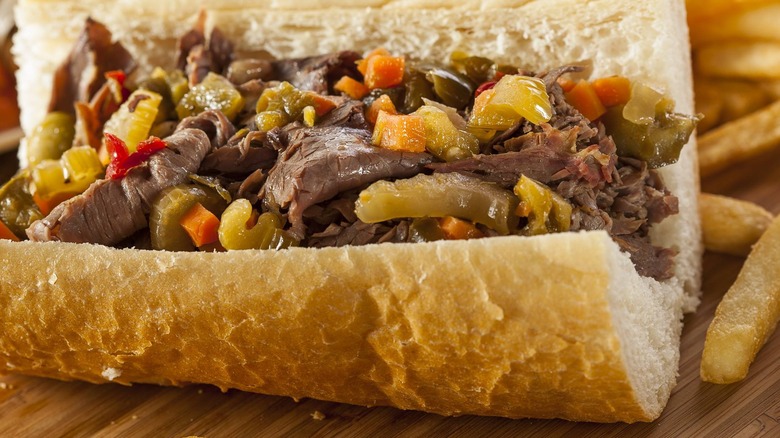 An Italian beef sandwich resting on a table. To the right are some fries.