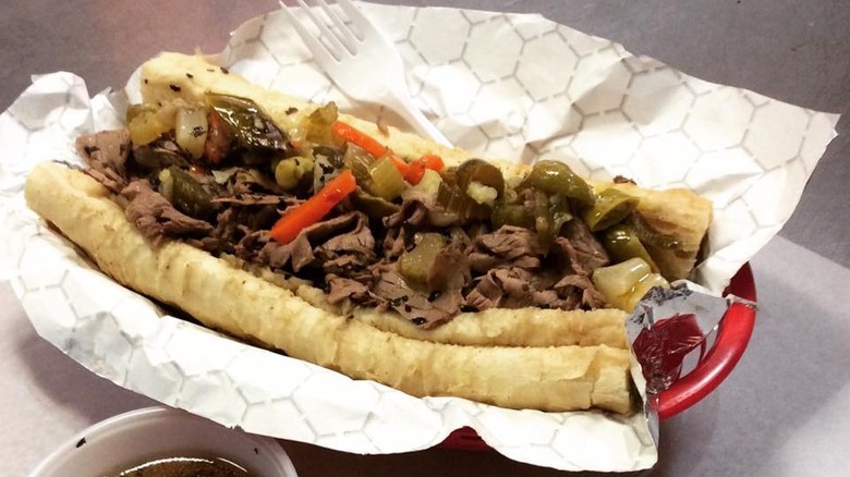 An Italian beef sandwich rests on a wrapper inside a basket. There is a plastic fork to the side.