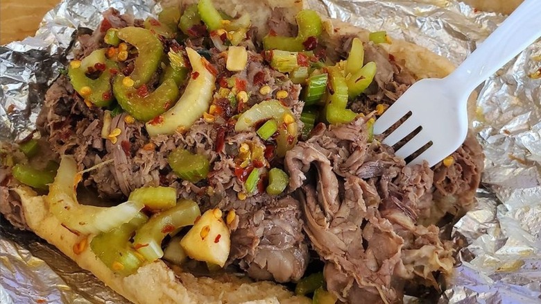 A Italian beef sandwich, sitting on aluminum foil with a plastic fork sticking out of it.