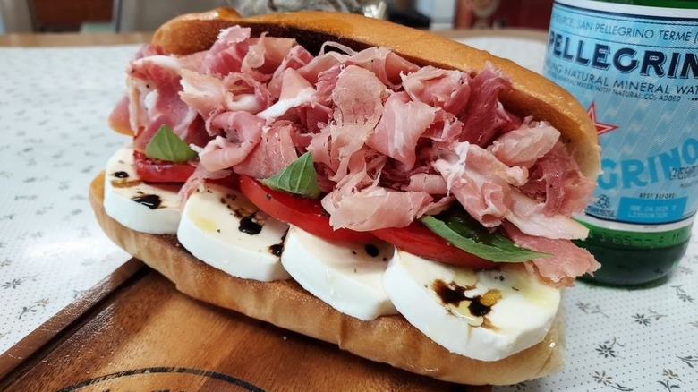 A special Italian "sammich" from Hagarville Grocery, featuring prosciutto and fresh mozzarella, sitting on a wooden cutting board and served with a bottle of Pellegrino