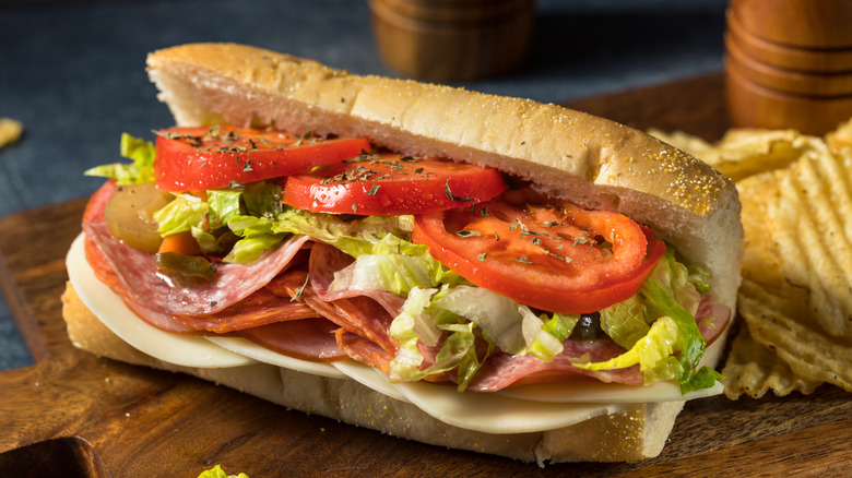 An Italian sub sandwich or hoagie on a wooden cutting board with potato chips