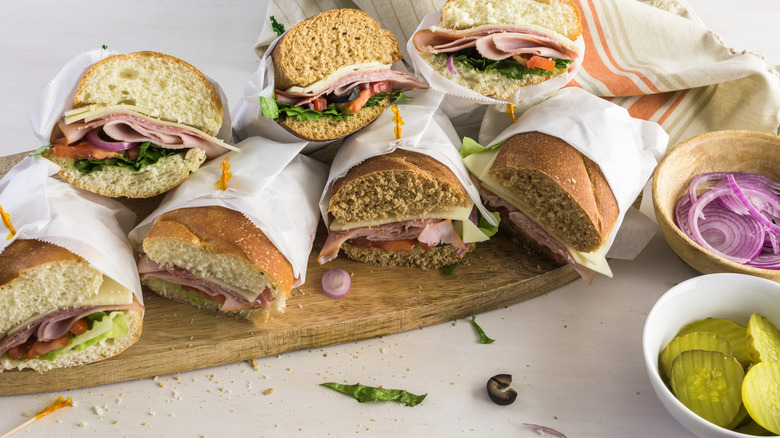 Fresh Italian sub sandwiches on white and wheat hoagie rolls stacked on top of a wooden cutting board