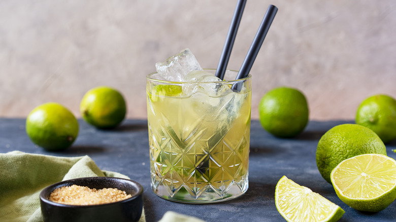 Caipirinha cocktail on a table surrounded with limes.