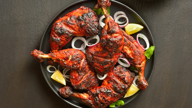 Grilled chicken legs on thighs on plate with rings of onion and lemon wedges.