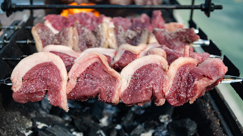 Raw picanha steaks skewered in a crescent shape with the fat cap to the outside.