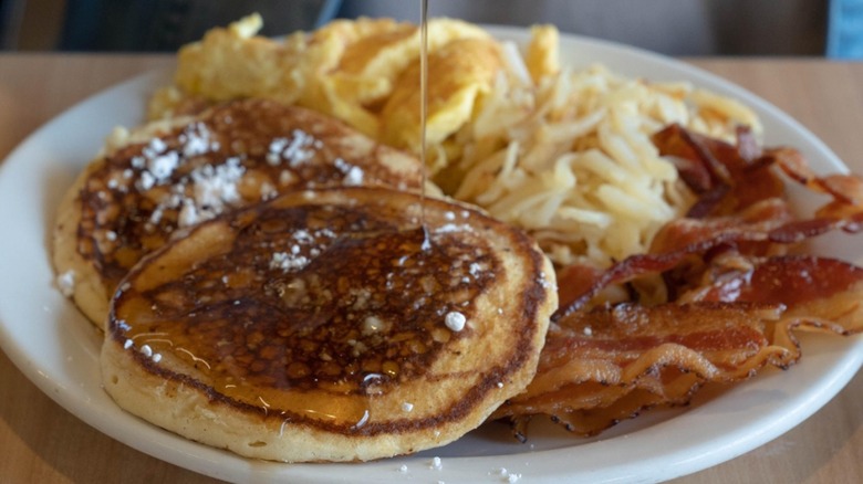 Golden Corral Pancakes with syrup being poured on them and powdered sugar and eggs and bacon and hash browns