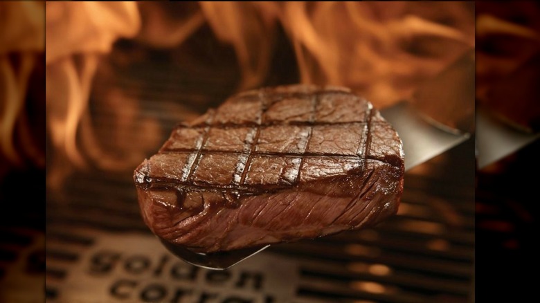 Golden Corral Sirloin Steak slab on spatula with flames in background blurred