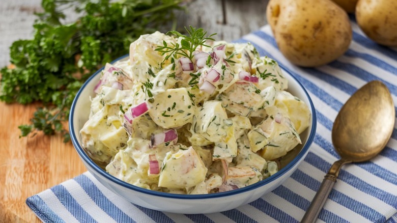 Potato salad in white bowl on blue and white striped cloth napkin