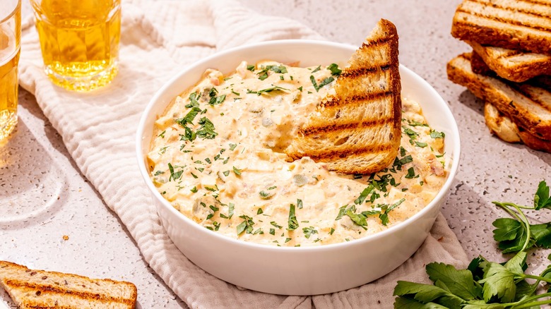 A slice of toasted bread dipped into a bowl of tuna salad