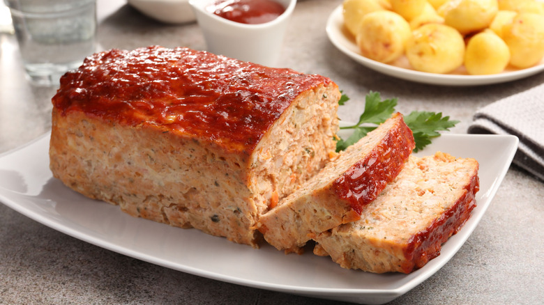 Whole turkey meatloaf sitting on a white plate with lemons in the background.