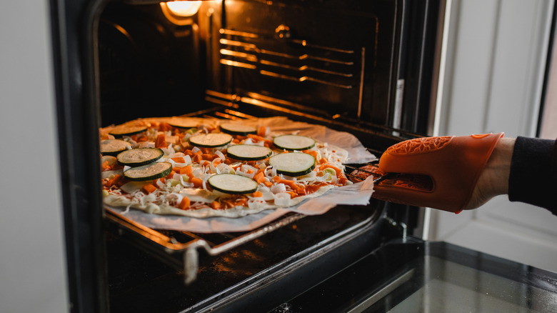 Hands adding a homemade pizza to the oven