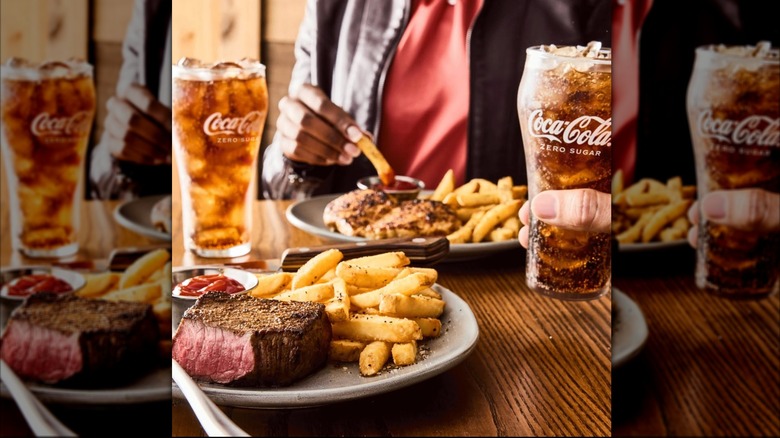A plate of steak and fries and one of chicken and fries with two glasses of Coke Zero