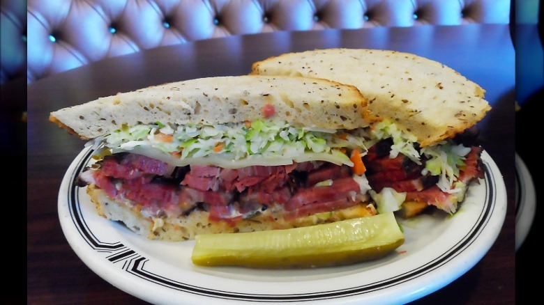 Close up of Langer's deli pastrami sandwich on white plate with lettuce, cheese, and pickle on side
