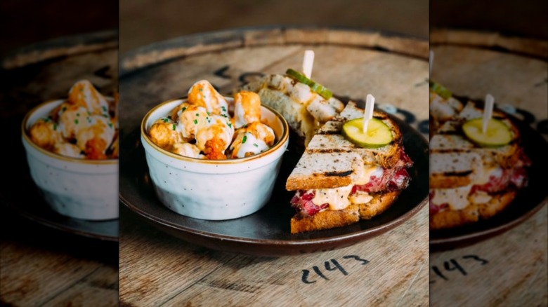 Cut artisan pastrami sandwich next to bowl of tater tots