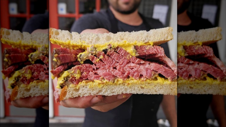 Man holding half of pastrami sandwich with mustard