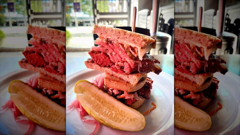 Two pastrami sandwich slices stacked on top of each other with half pickle