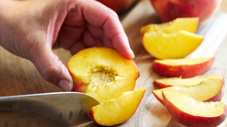 A person holding a knife while slicing peaches