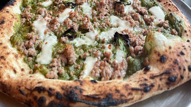 Close up of pizza with pesto, mozzarella, and ground meat