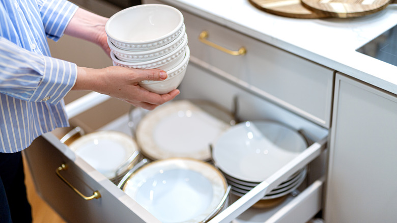Person lifting a stack of bowls above a drawer filled with dishes