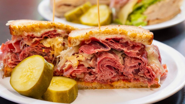 A Reuben sandwich with pickles on white plate