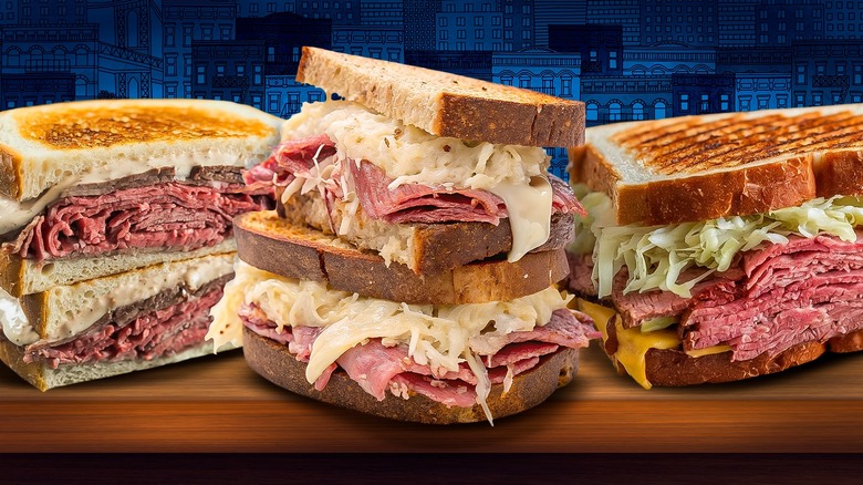 Three Reuben sandwiches with corned beef, swiss cheese, sauerkraut, and russian dressing, on rye bread.